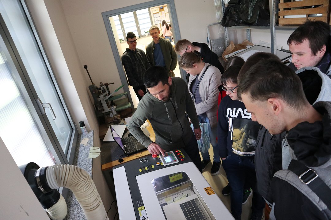 Na sliki so učenci OŠ Kozara, ki si ogledujejo kako deluje gravirni stroj
