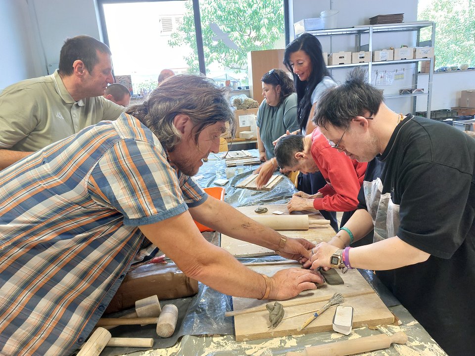 Mentor in uporabniki v delavnici ustvarjajo keramične ploščice